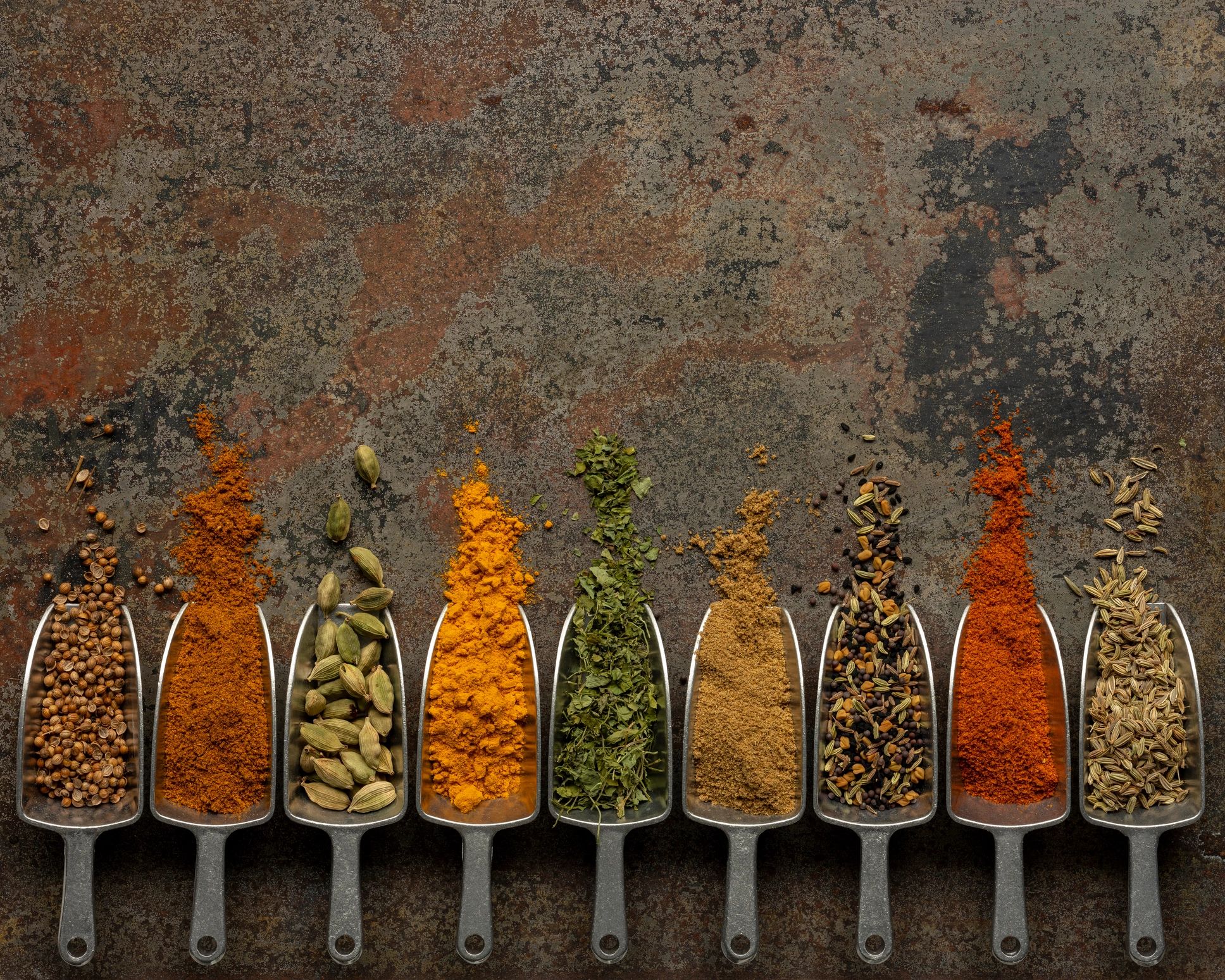 Colorful spice scoops arranged on a rustic metal surface