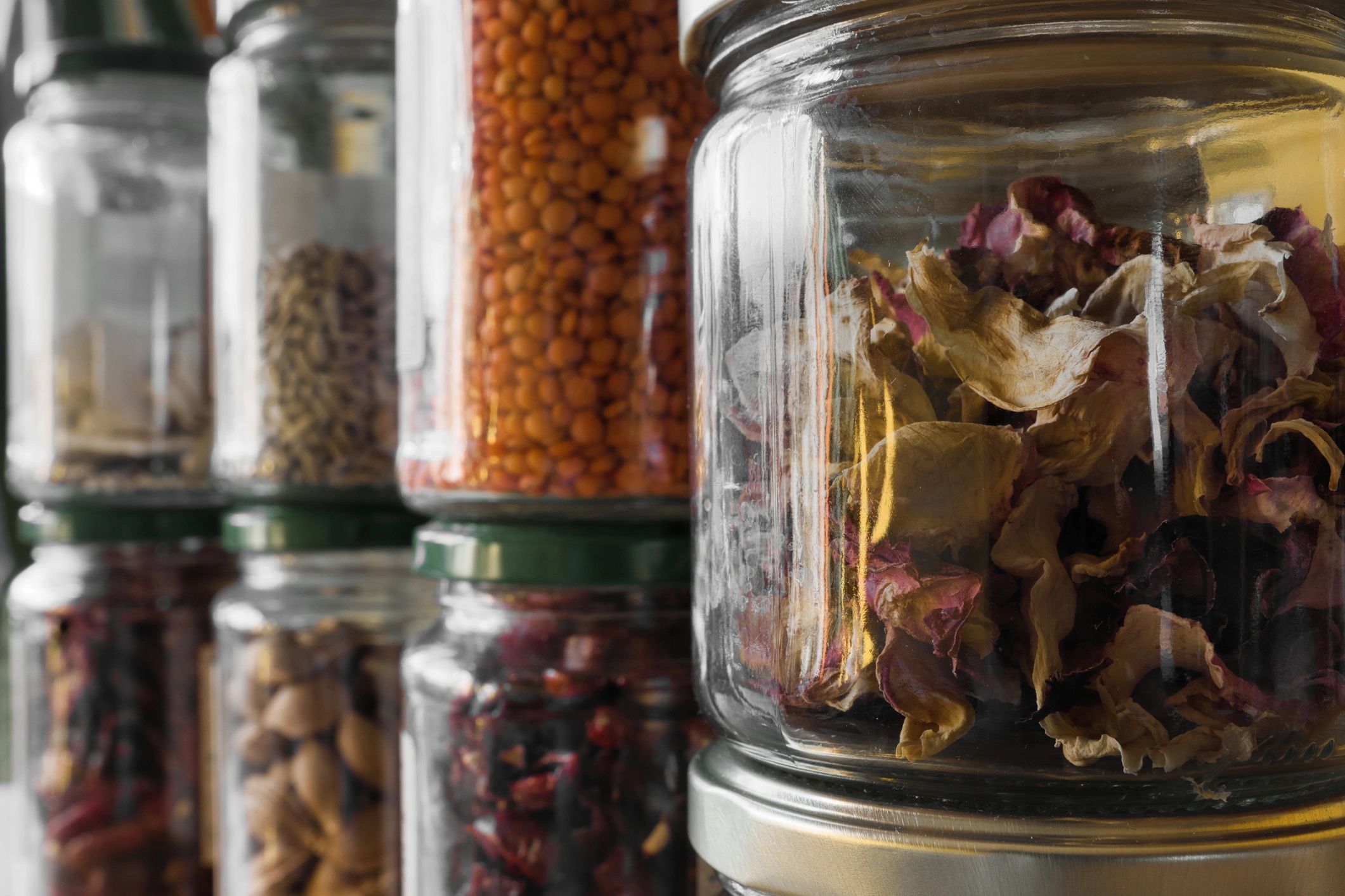 Arrangement of herbs, legumes and dried rose petals lined up in glasses